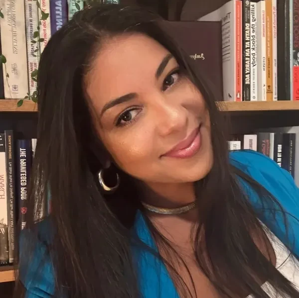 A woman smiling warmly with bookshelves in the background.