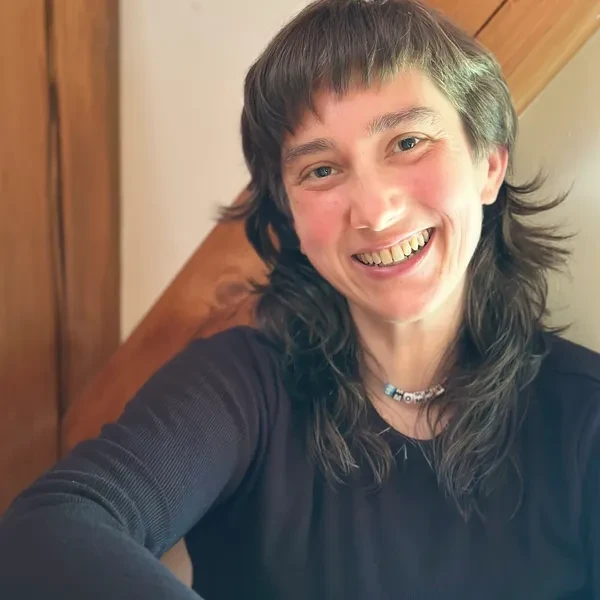 Smiling person with layered hair and a necklace, wearing a black top.